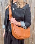 Woman wearing a denim jacket and black dress, holding a dark tan crossbody handbag.