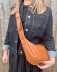 Woman wearing a denim jacket and black dress, holding a dark tan crossbody handbag.