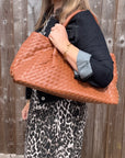 woman wearing a denim jacket and leopard print dress holding a dark tan woven handbag