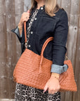 woman wearing a denim jacket and leopard print dress holding a dark tan woven handbag