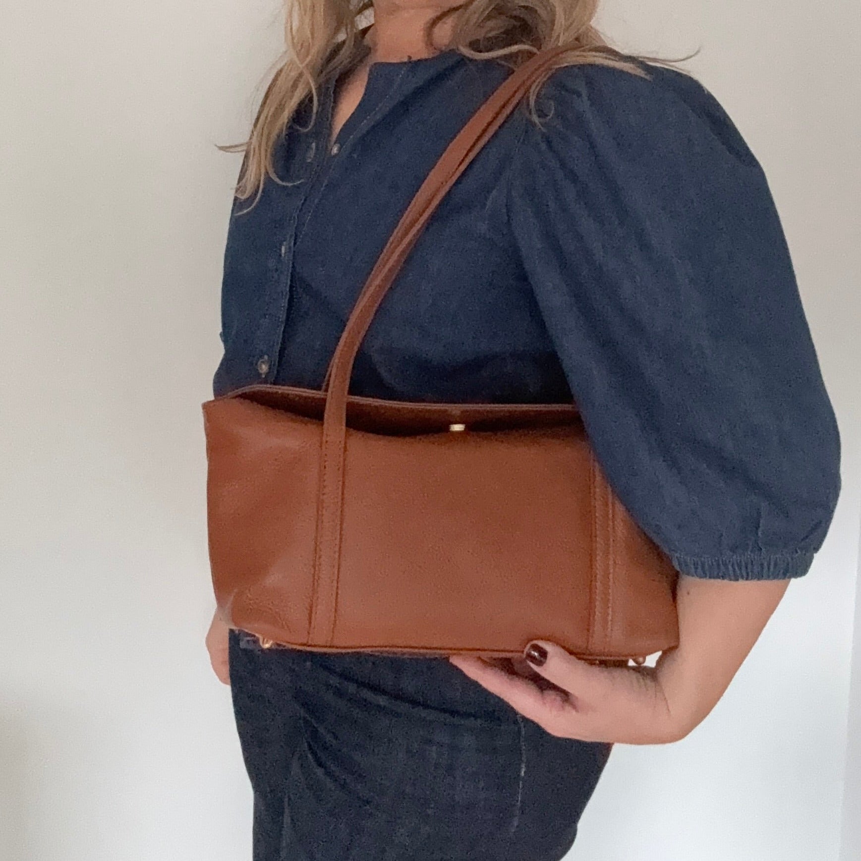 woman holding a dark tan leather  shoulder handbag 