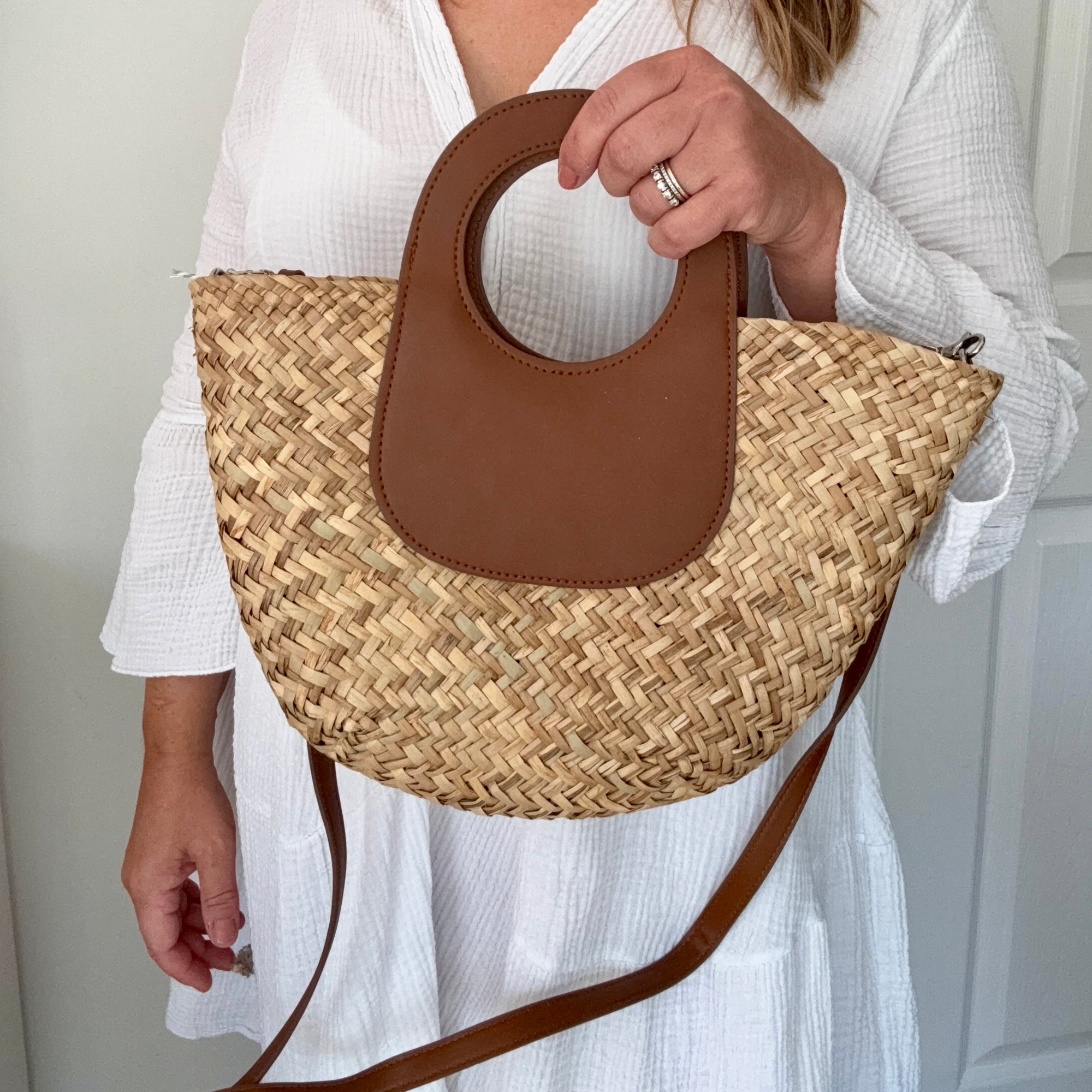 woman holding a straw handbag with brown leather accents