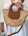 woman holding a straw handbag with brown leather accents