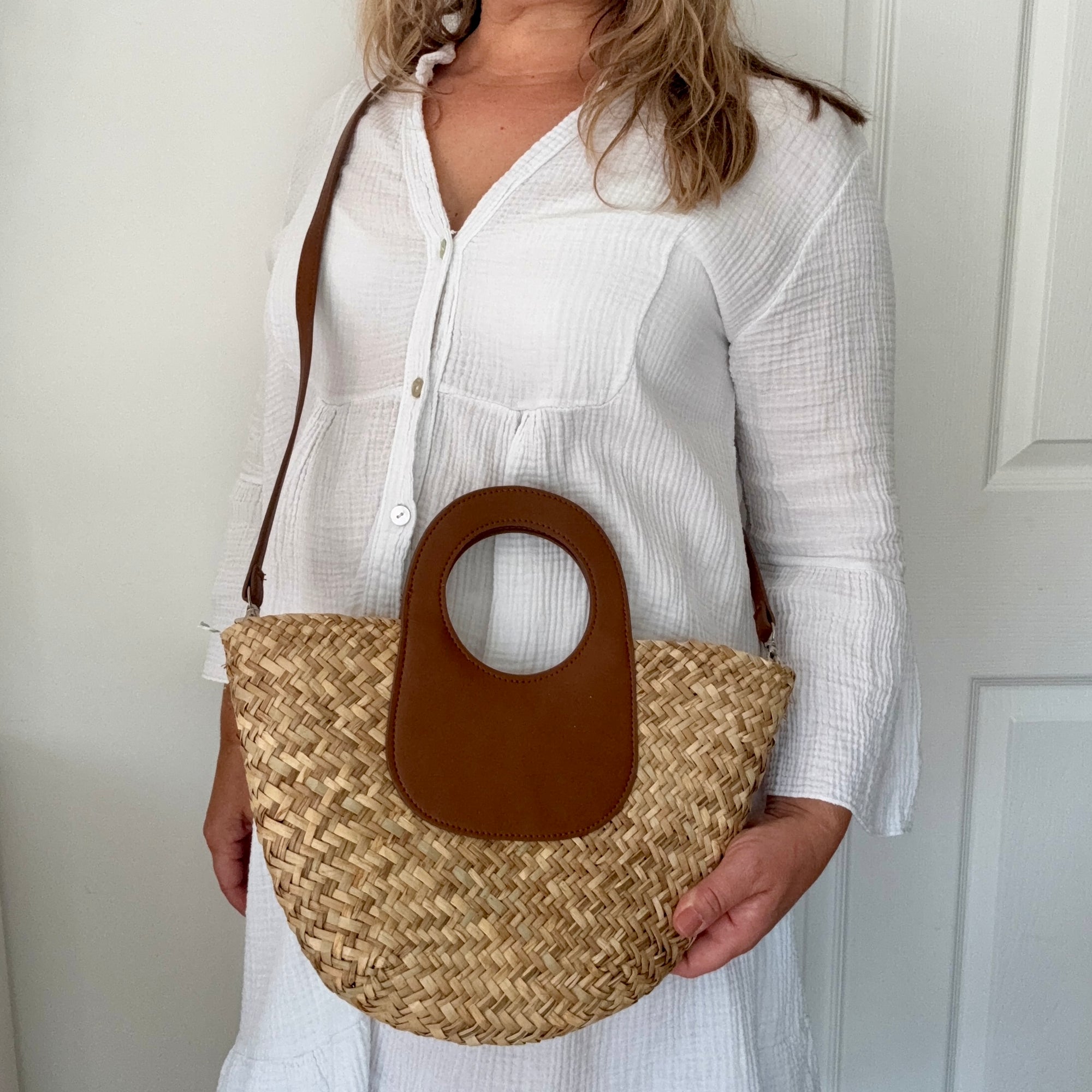 woman holding a straw handbag with a brown handle against a white background