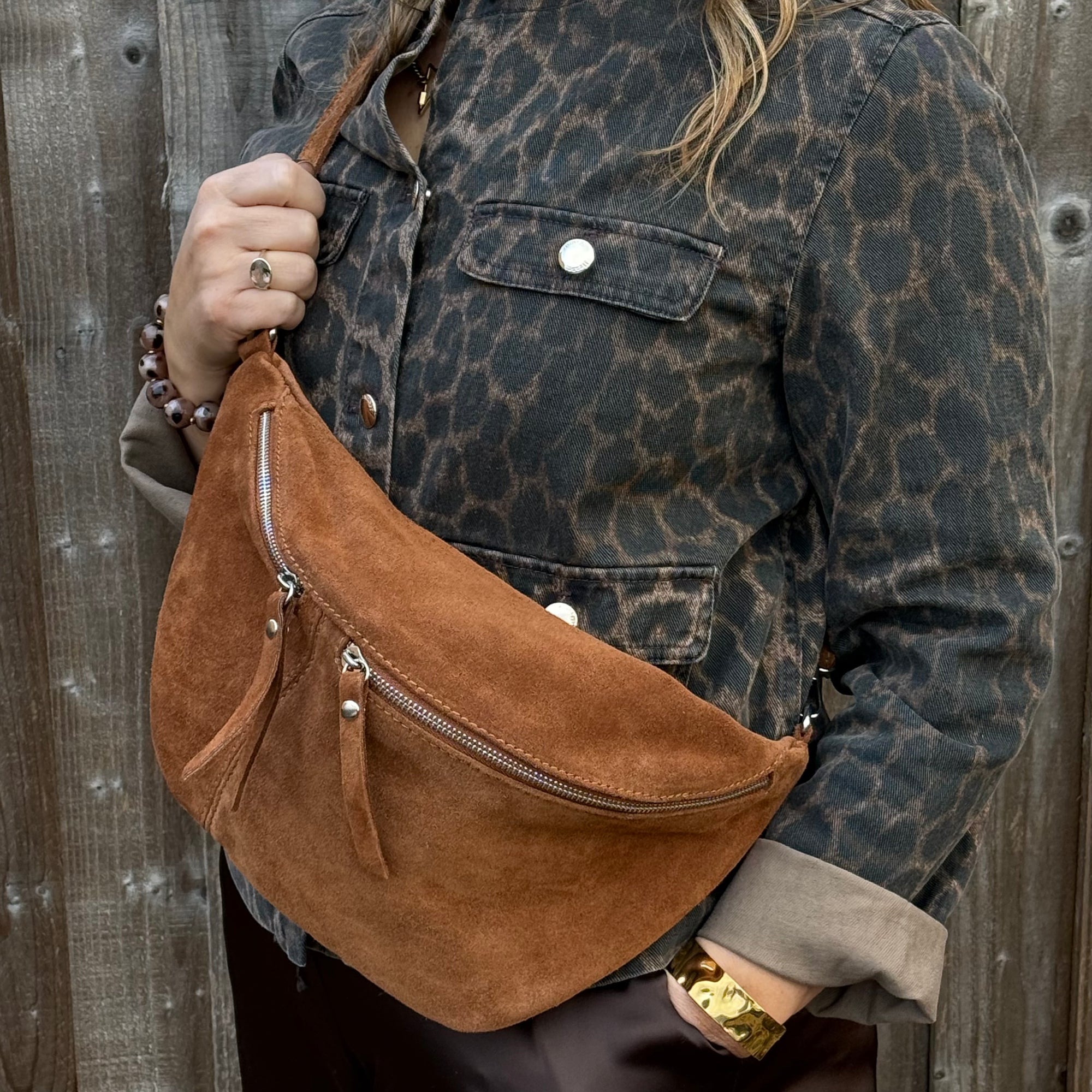 Person holding a large dark tan  suede bag and a brown leather jacket