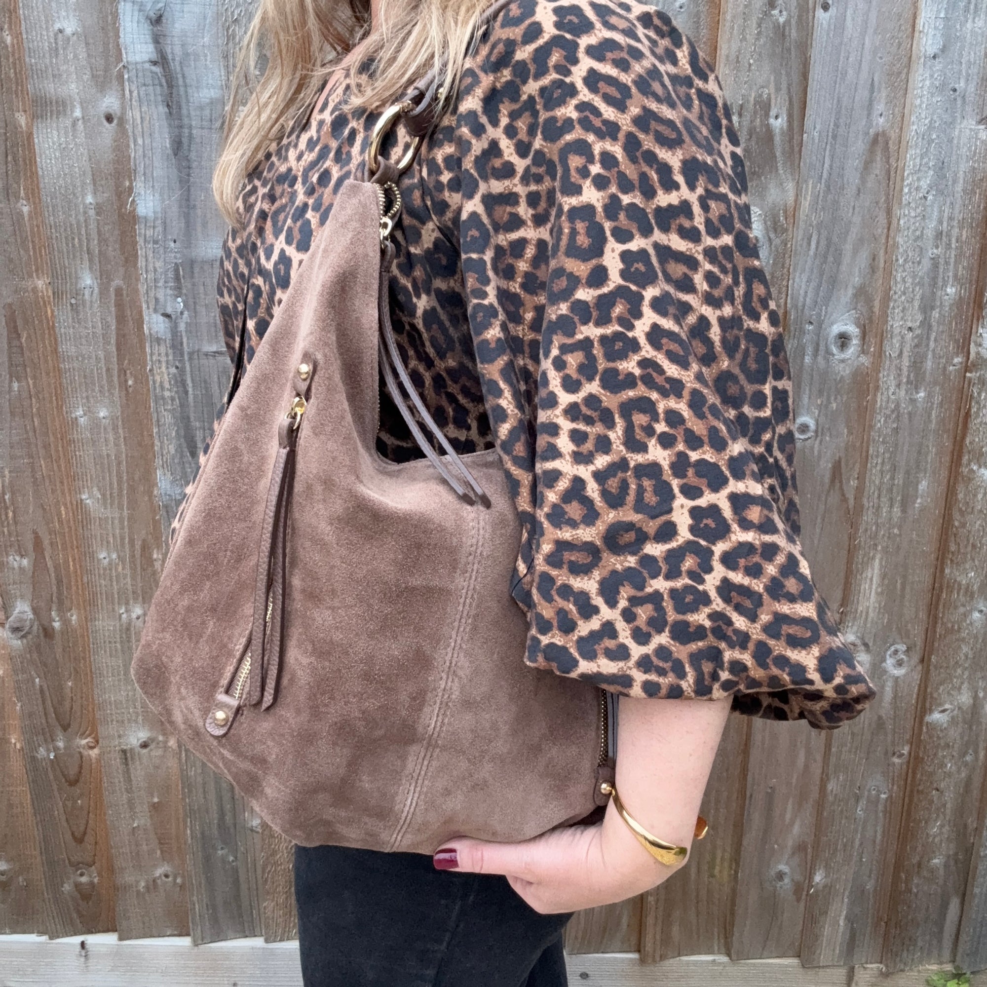 Lady wearing a leopard print top holding a taupe suede shoulder bag with leather trim