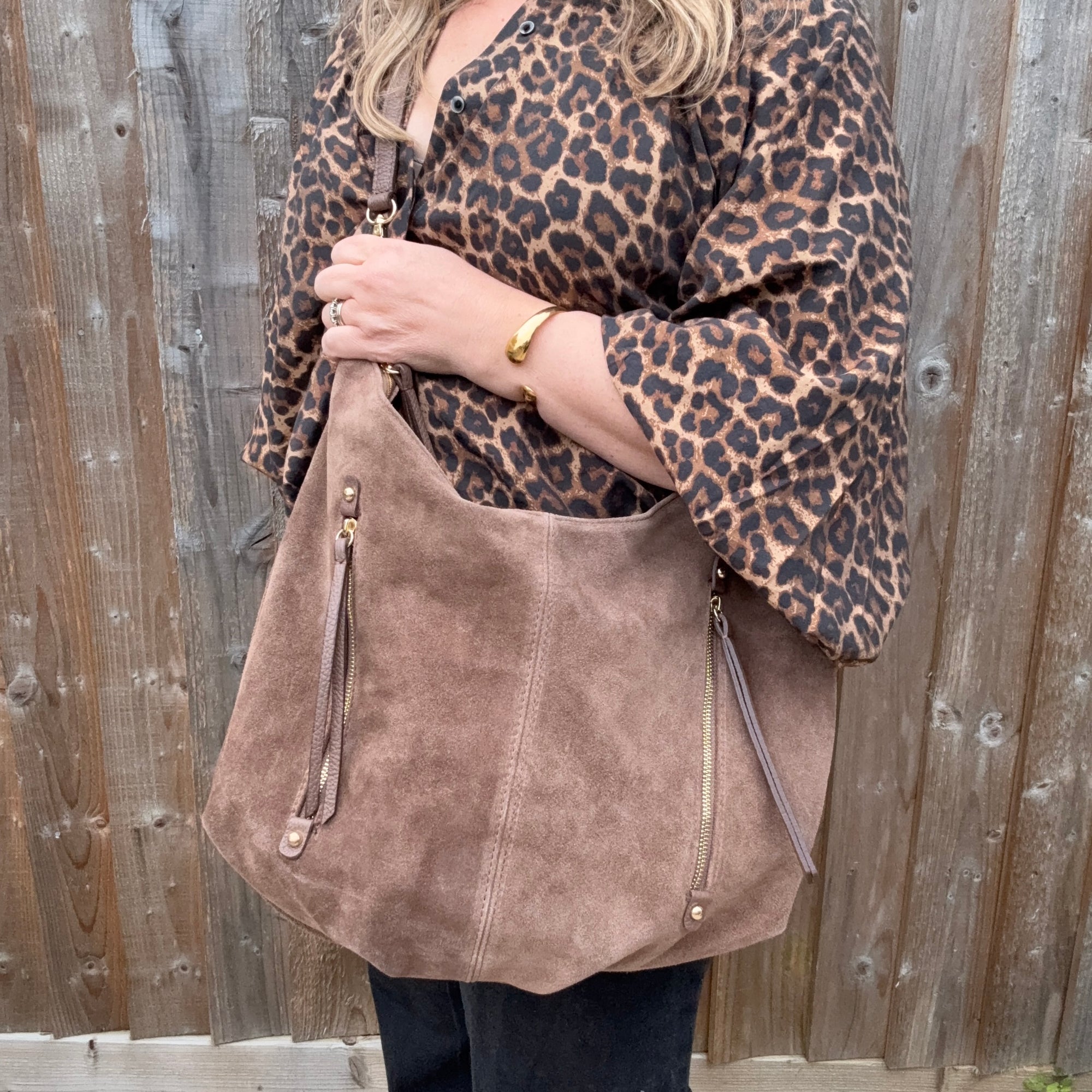 Woman wearing a leopard print top and holding a taupe suede crossbody bag with leather trims