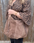Woman wearing a leopard print top and holding a taupe suede crossbody bag with leather trims