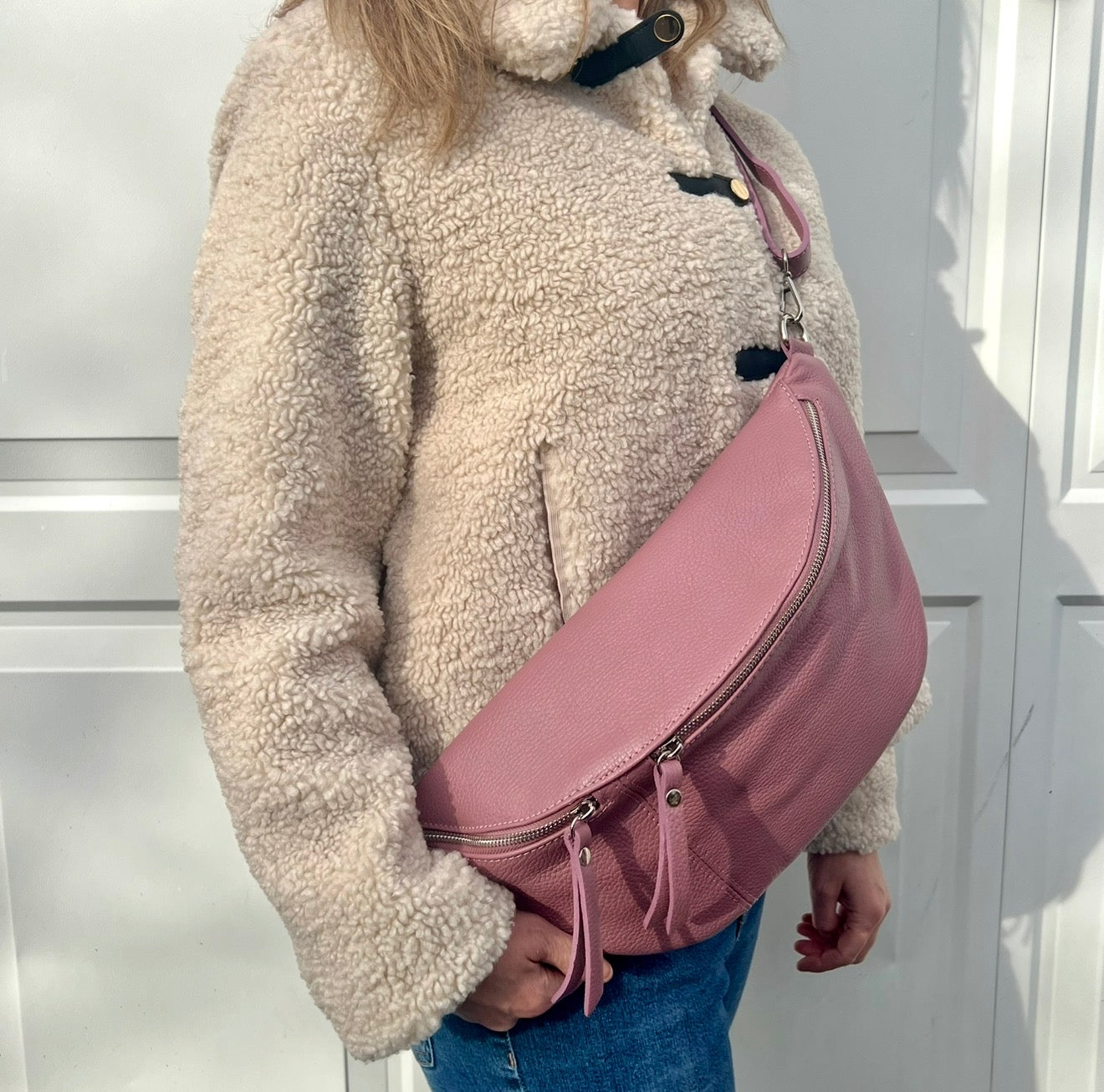 Woman wearing a beige fleece jacket with a pink crossbody bum handbag. 