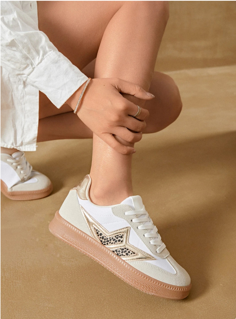 A person wearing white leopard print trainers with gold stars, paired with light-colored shorts.