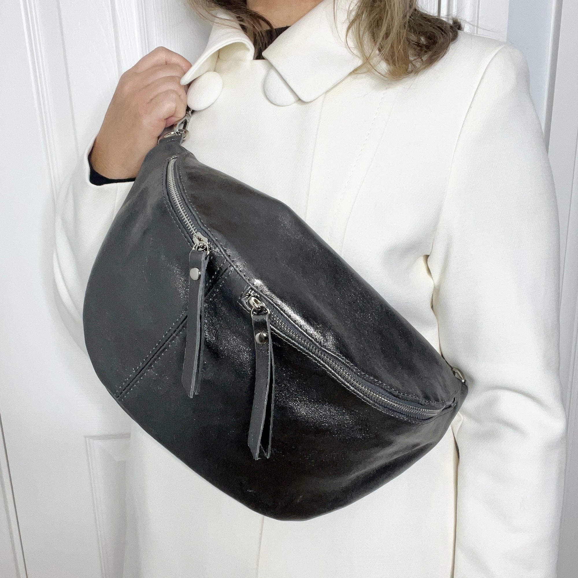 A person wearing a white coat holding a pewter large crossbody bum bag with a detachable leather strap.