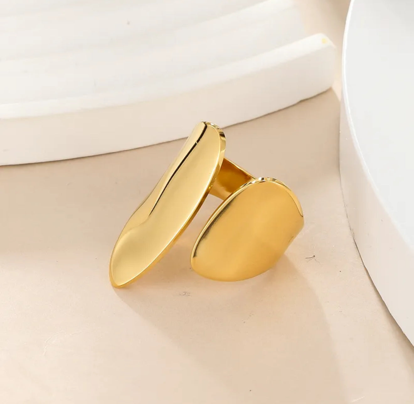 Gold chunky adjustable ring on a beige surface with a white background