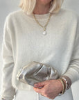 A woman  wearing a light grey sweater holding a silver clutch against a neutral background