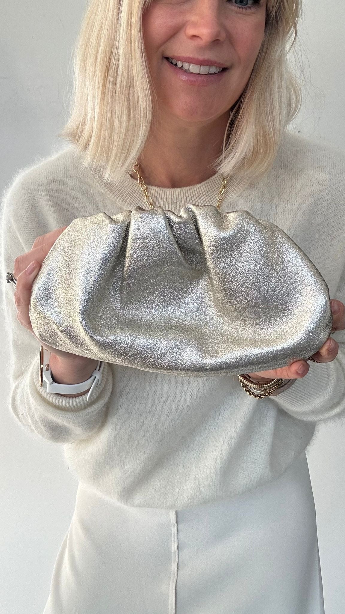 woman holding a gold clutch against a plain background