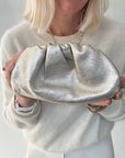 woman holding a gold clutch against a plain background