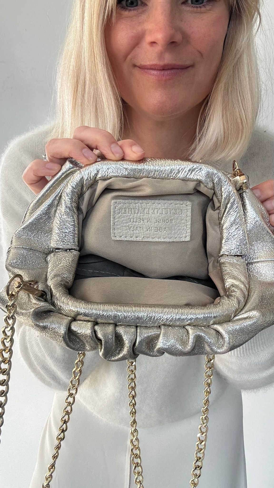 Person holding a gold clutch handbag with gold chains against a neutral background
