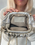 Person holding a gold clutch handbag with gold chains against a neutral background