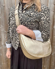 Woman wearing a leopard print jacket holding a gold crossbody handbag. 