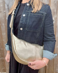 Woman wearing a denim print jacket holding a gold crossbody handbag. 