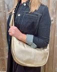Woman wearing a denim print jacket holding a gold crossbody handbag. 