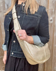 Woman wearing a denim print jacket holding a gold crossbody handbag. 