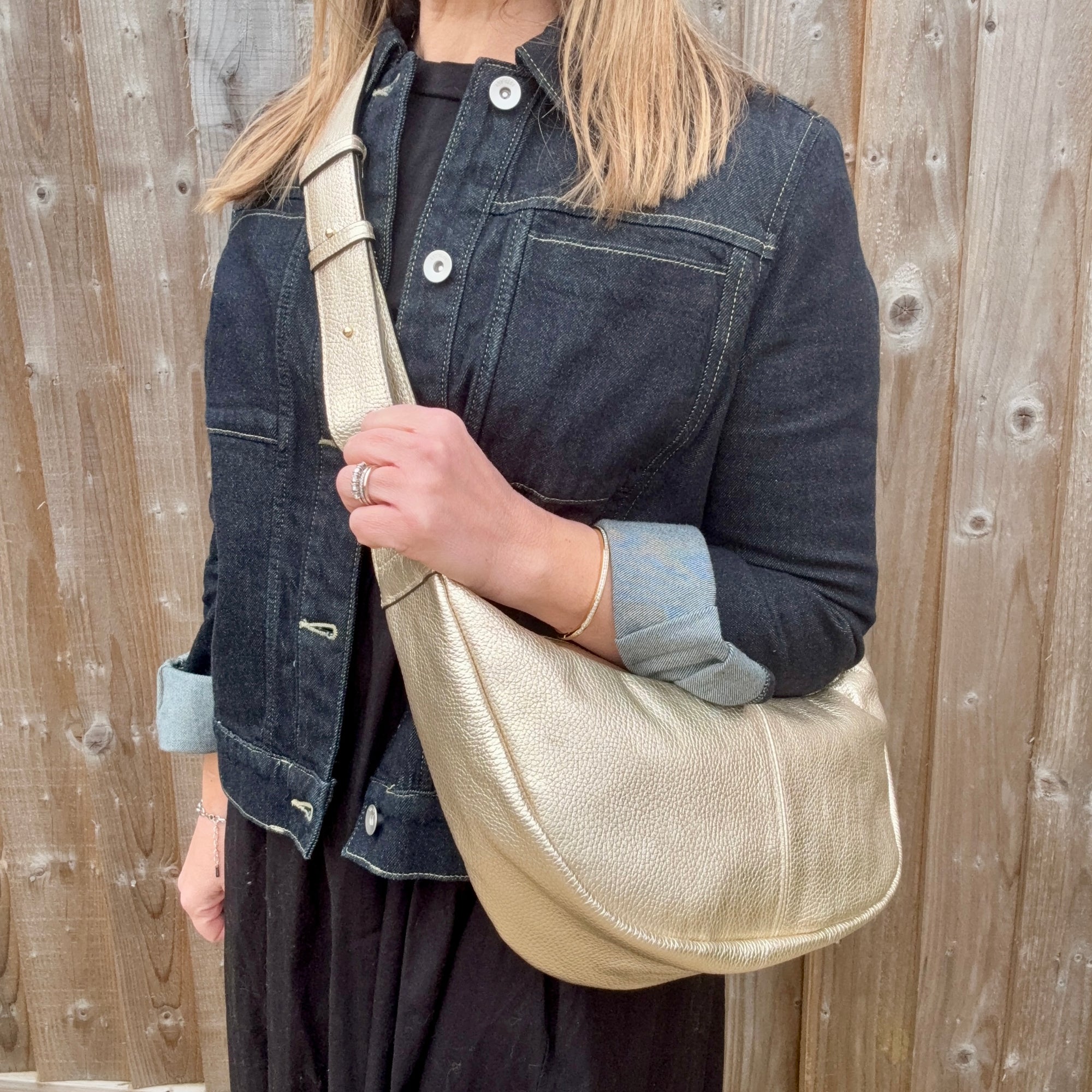 Woman wearing a denim print jacket holding a gold crossbody handbag. 