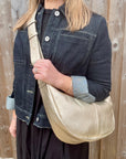 Woman wearing a denim print jacket holding a gold crossbody handbag. 