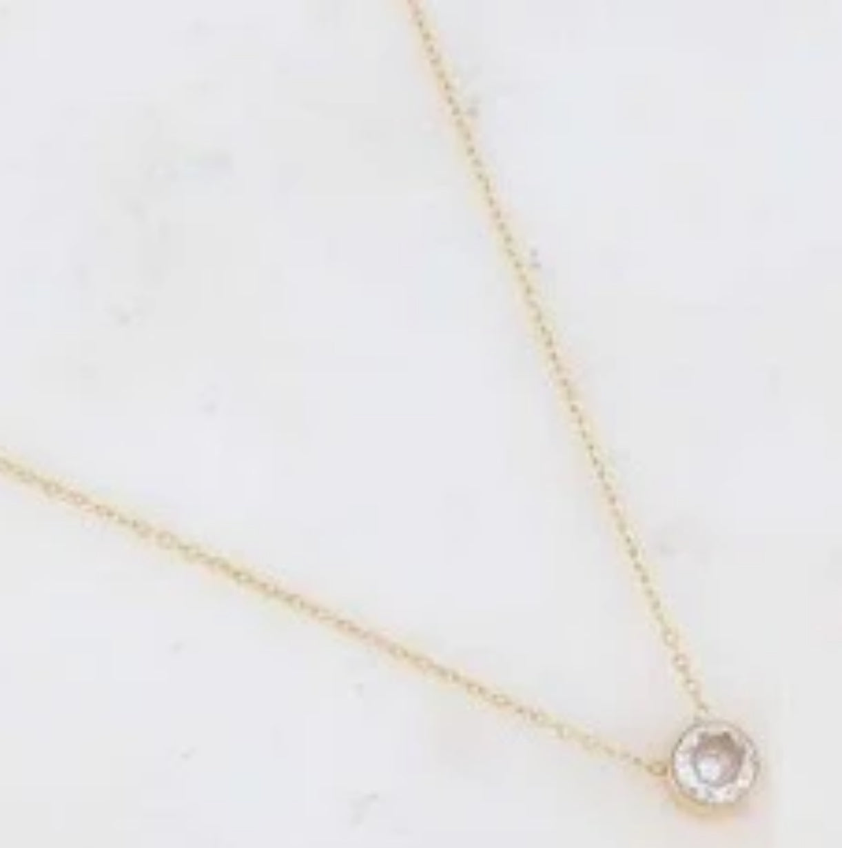 Gold necklace with a clear pendant on a light background