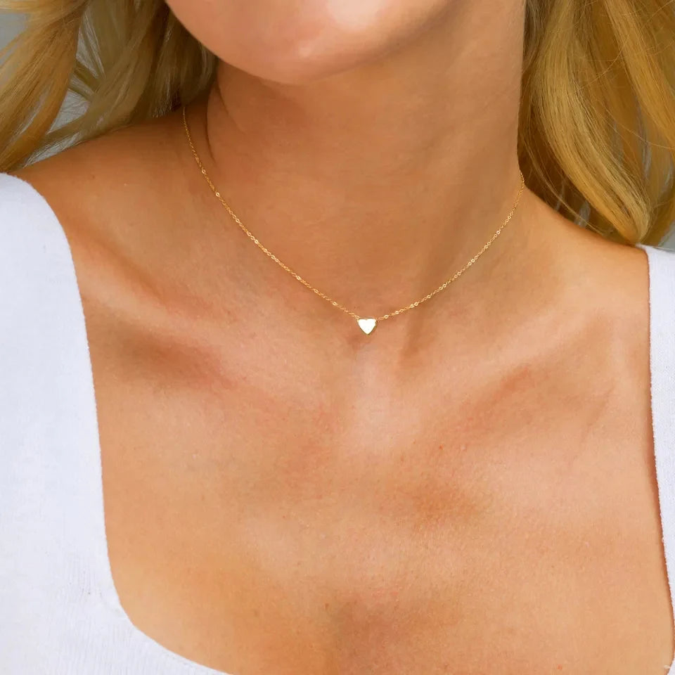 A woman wearing a white v-neck top and a gold delicate heart necklace with a extension chain.