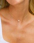 A woman wearing a white v-neck top and a gold delicate heart necklace with a extension chain.