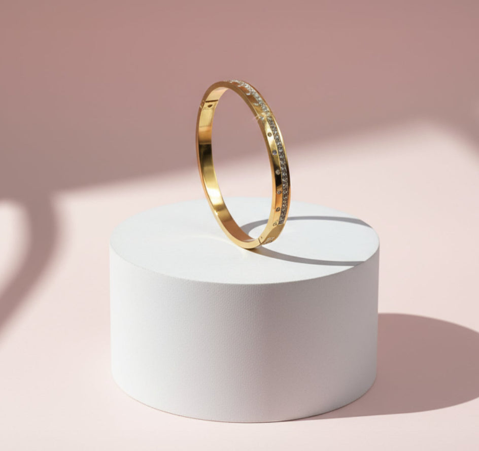 Gold bracelet on a white cylindrical stand.