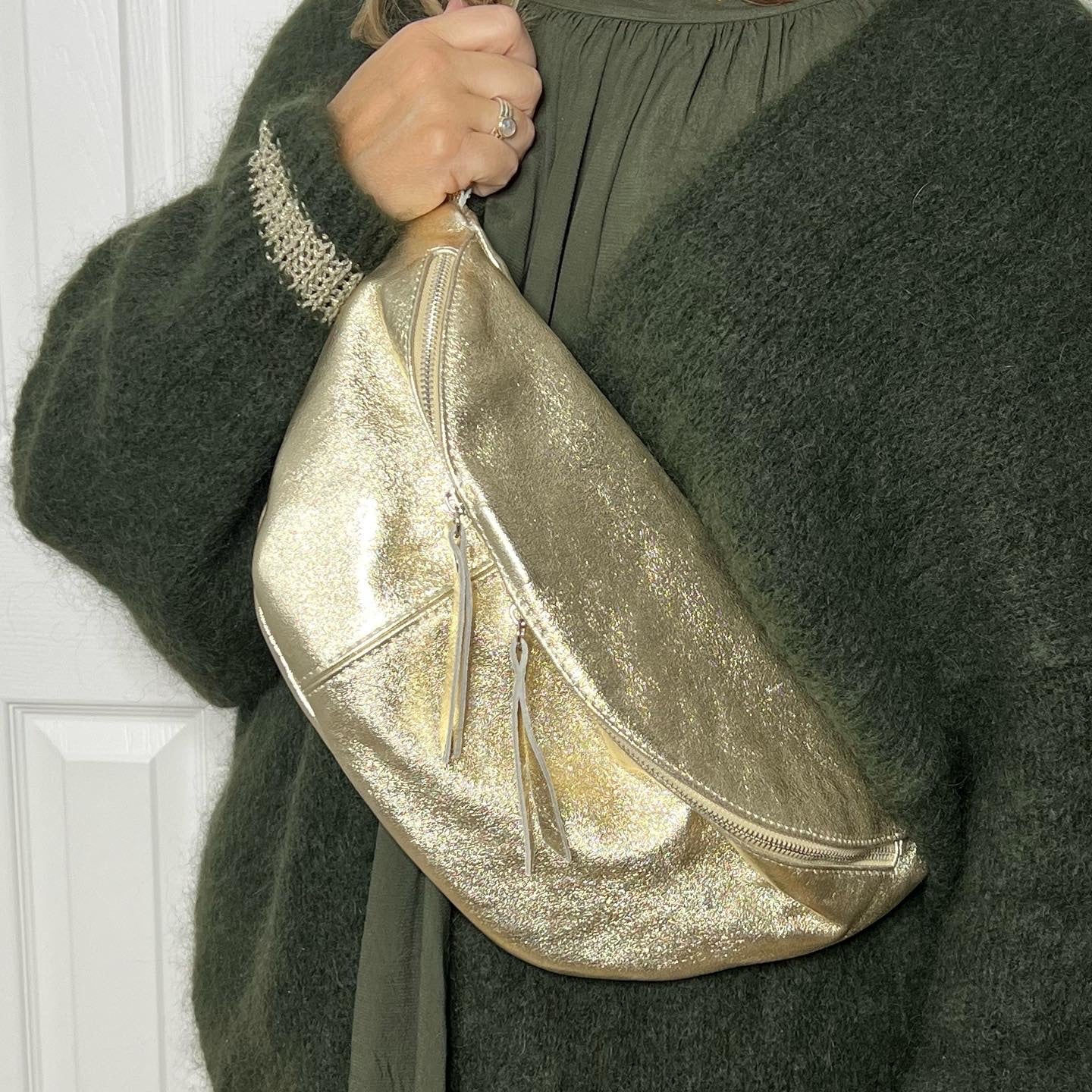 woman wearing a green cardigan holding a large gold crossbody bum bag. 