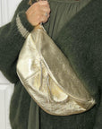 woman wearing a green cardigan holding a large gold crossbody bum bag. 