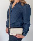 Woman wearing a blue denim shirt holding a gold clutch bag handbag with a gold accented chain. 