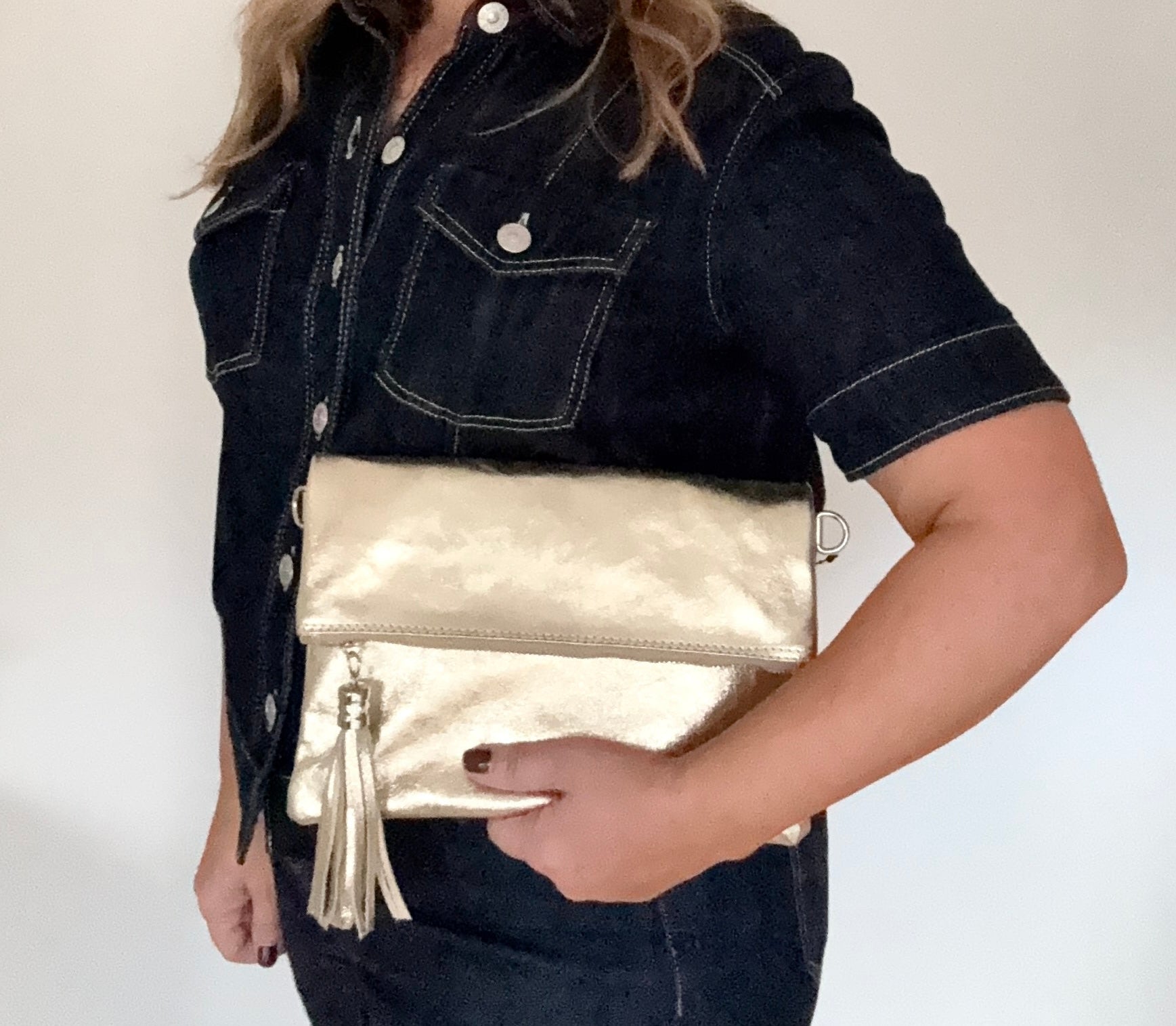 Woman holding a gold leather clutch/ crossbody  bag  with a gold tassel against 