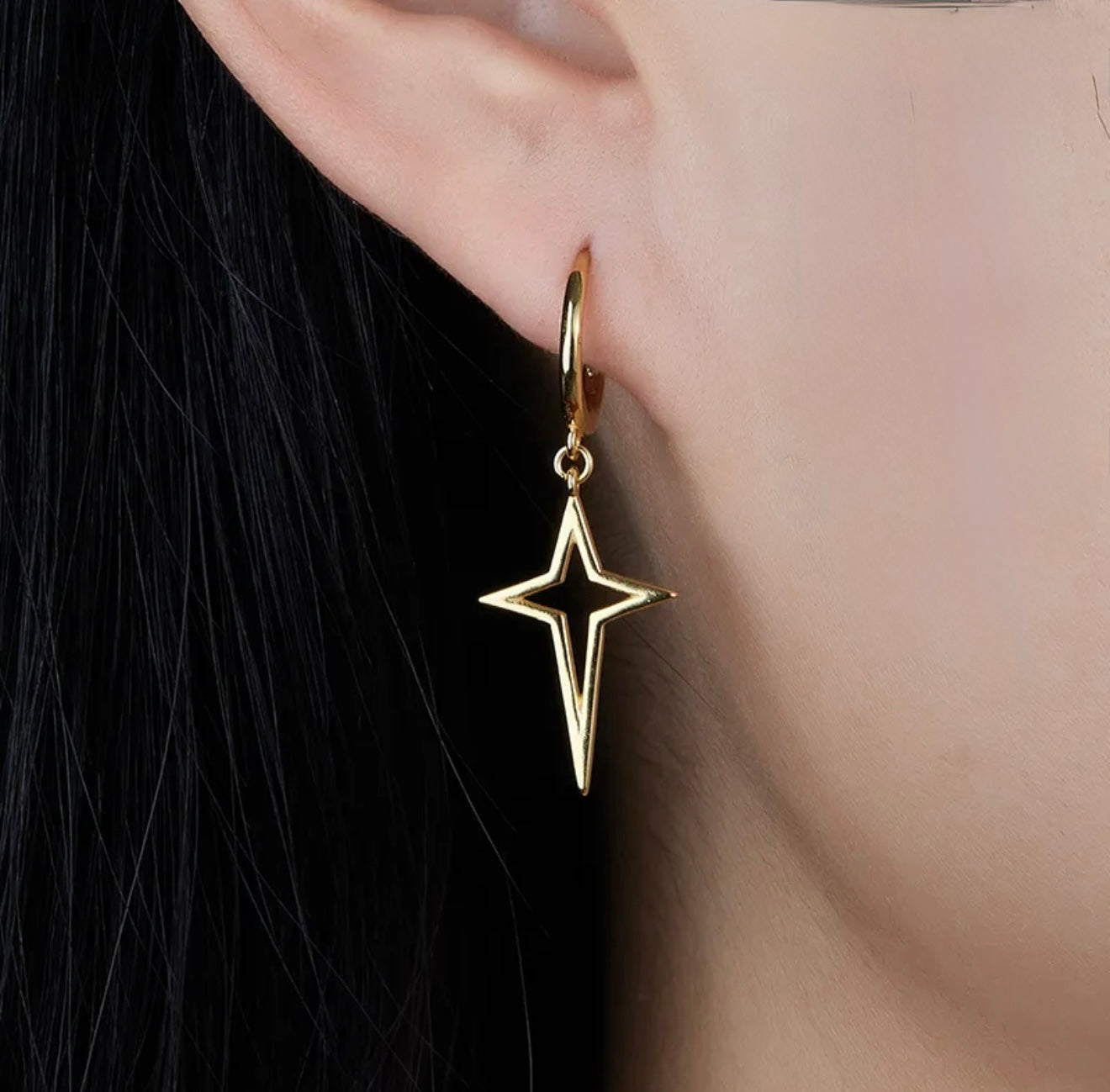 Gold star-shaped earring worn on an ear 