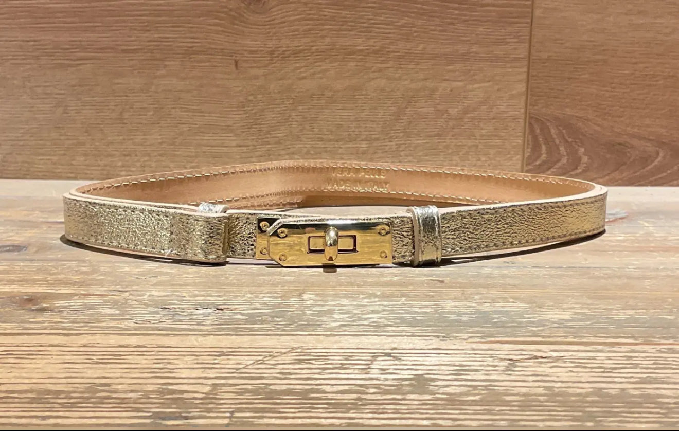 Gold narrow leather belt with a gold buckle on a wooden surface