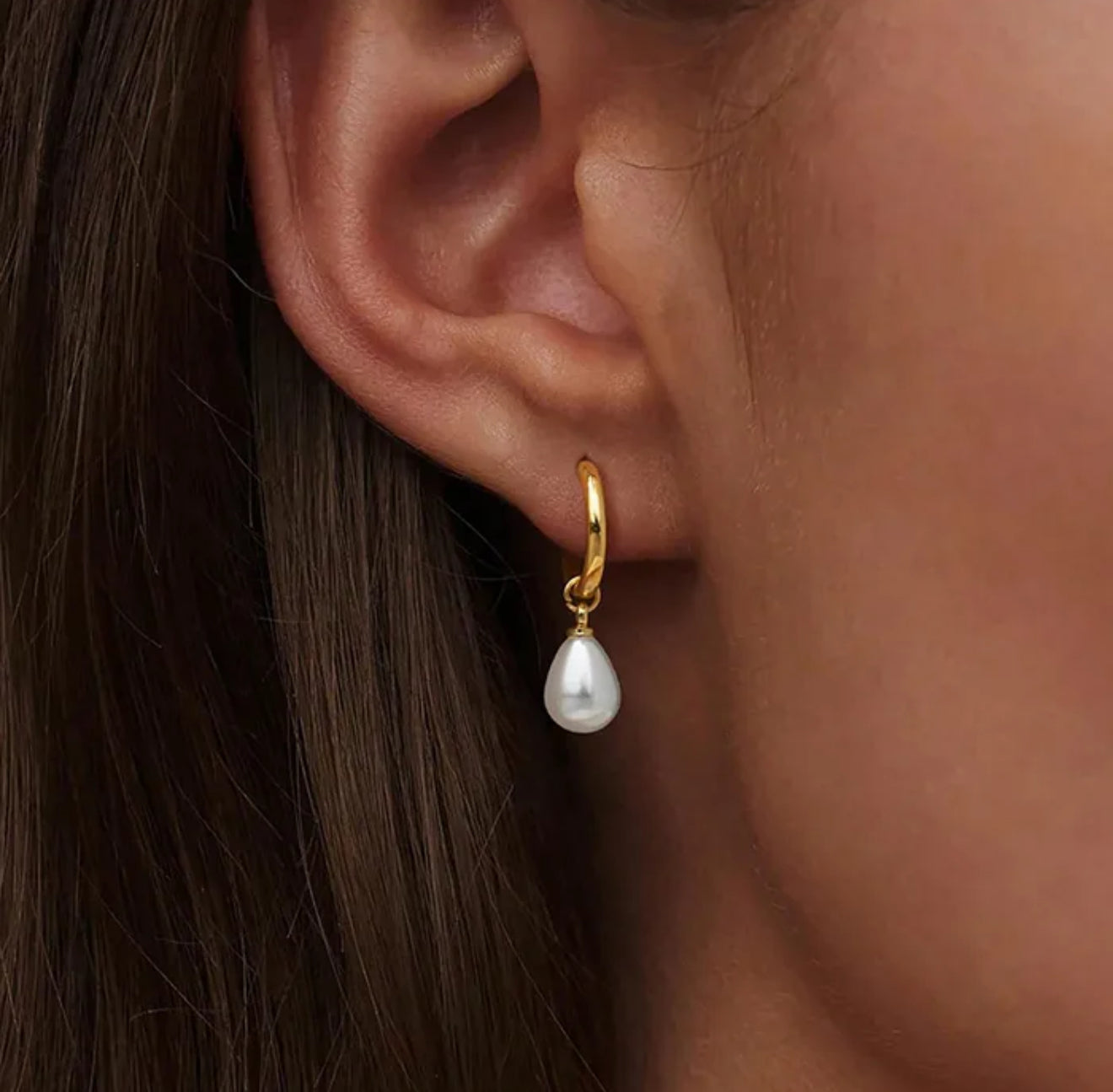 close up of woman wearing a gold pearl hoop drop earring.

