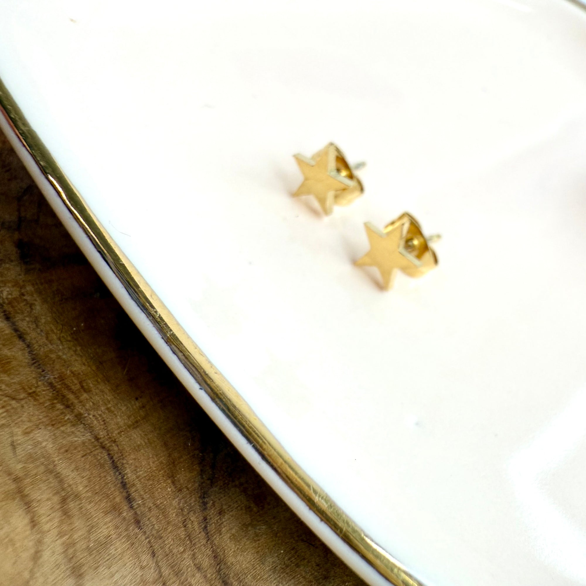 Gold star-shaped earrings on a white surface with a wooden background