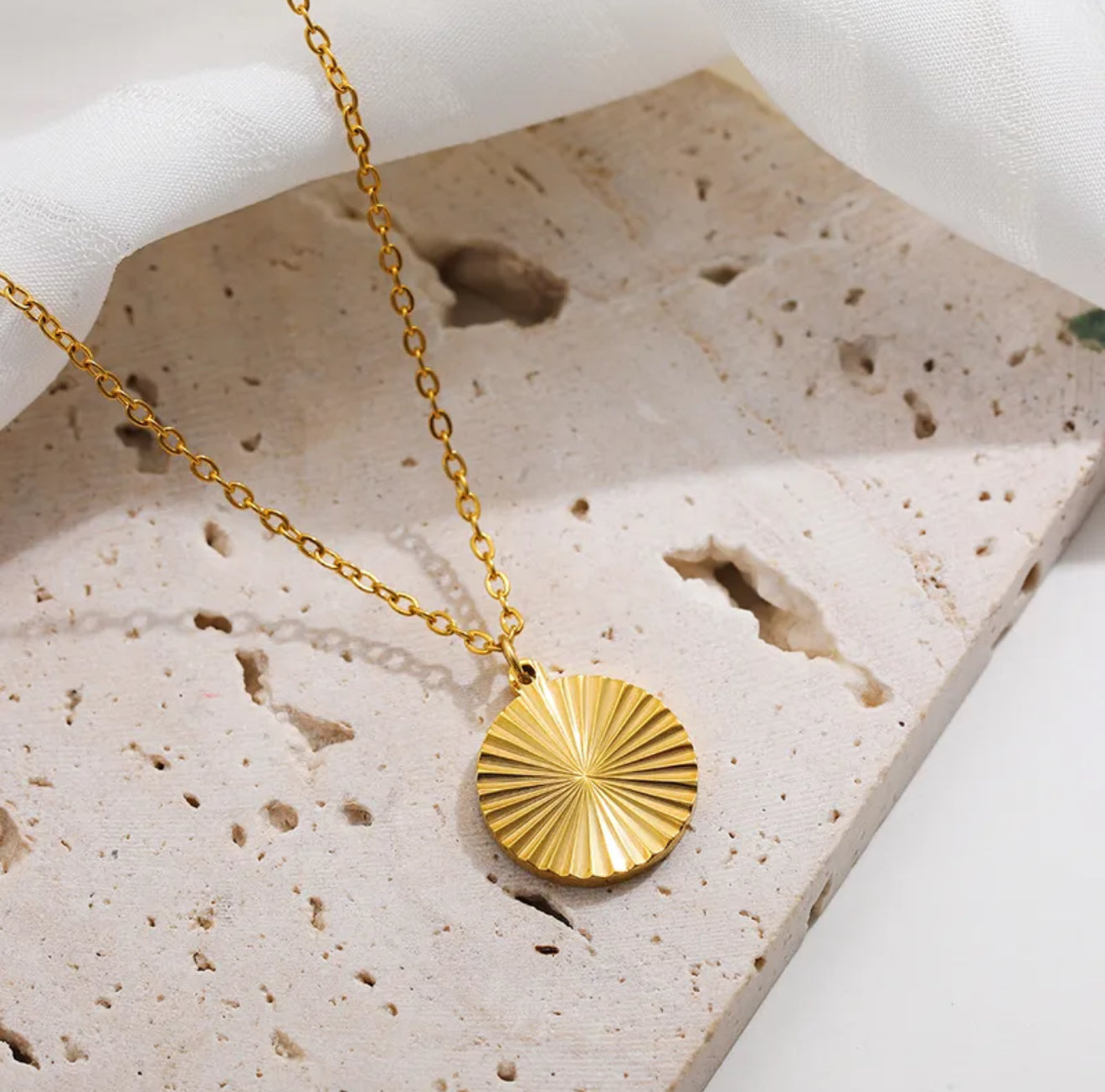 Gold textured necklace with a sunburst pendant on a textured stone surface