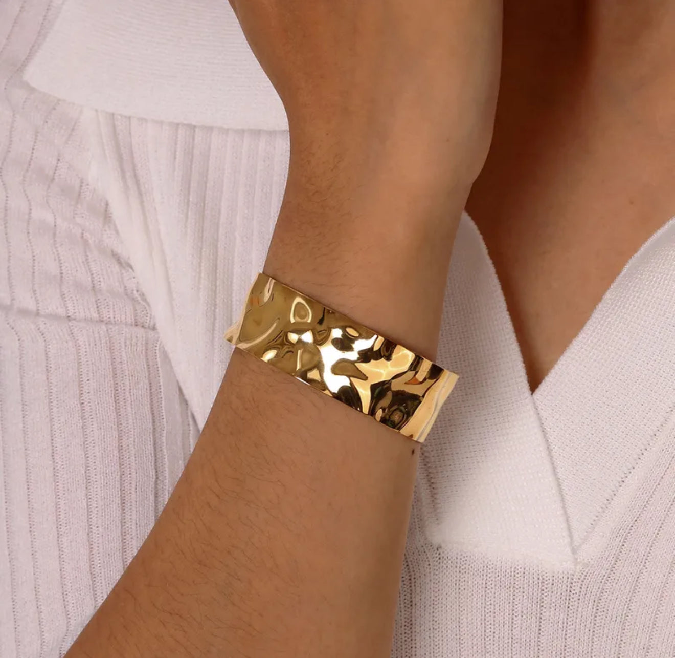 Gold textured cuff bangle bracelet on a wrist with a white background