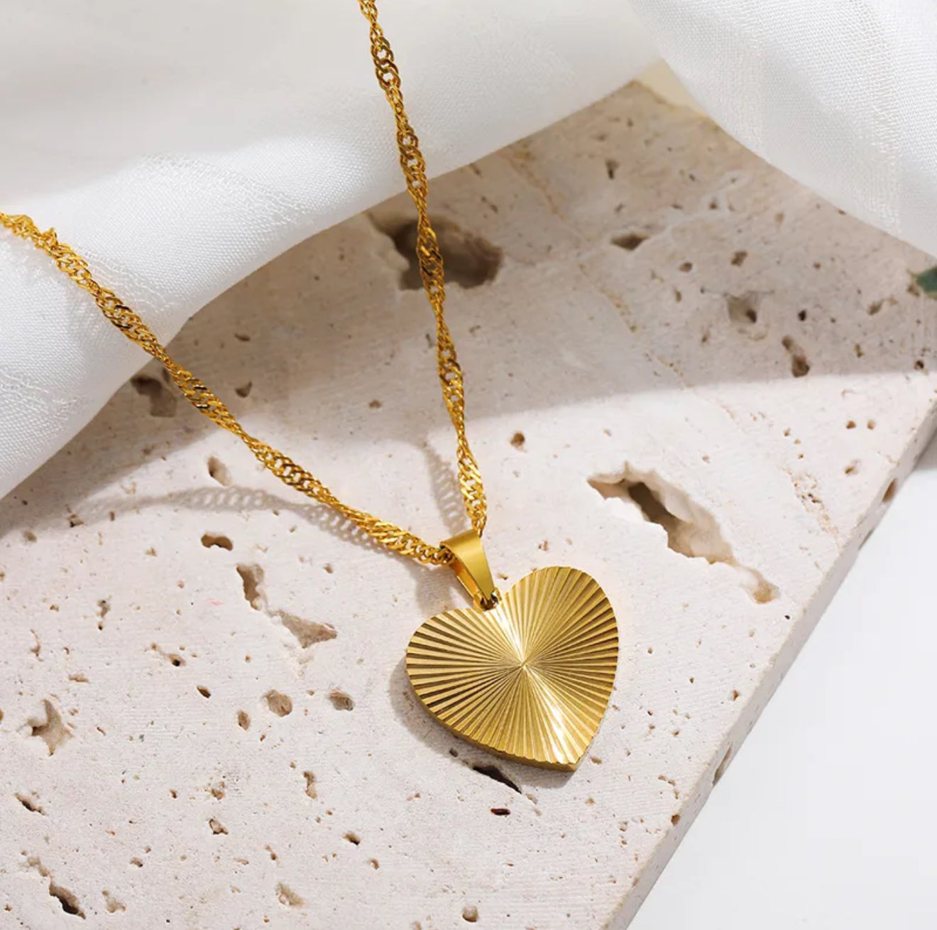 Gold textured heart-shaped pendant necklace on a textured stone surface