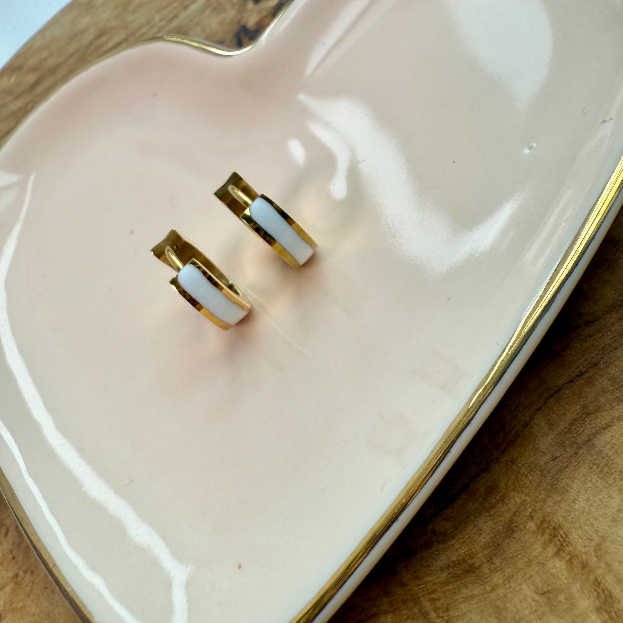 Gold and white earrings on a white dish 