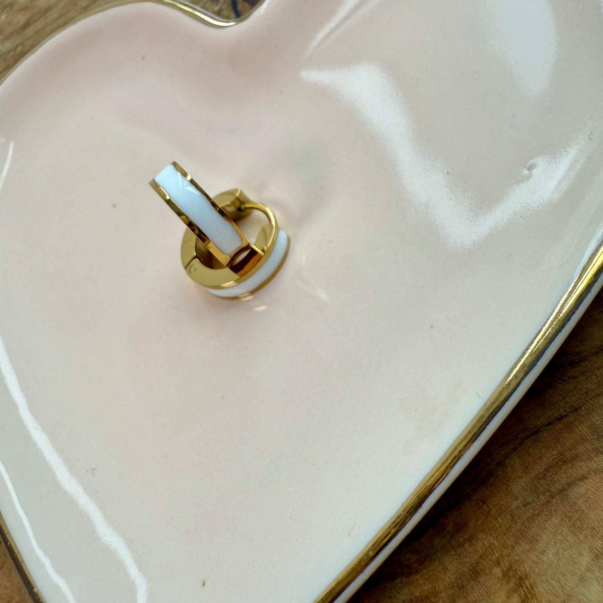 Close-up of a gold ring on a white ceramic plate with a wooden surface underneath.