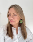 Woman wearing a white shirt with green and gold beaded disc earring.