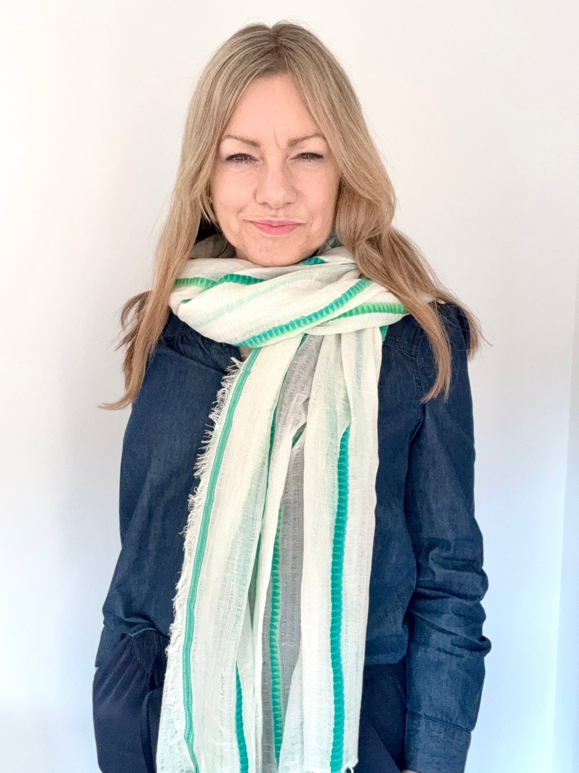 Woman wearing a green and white striped scarf over a denim shirt.