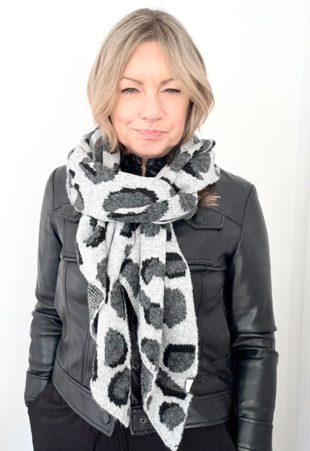 Person wearing a  grey animal print patterned scarf and leather jacket 