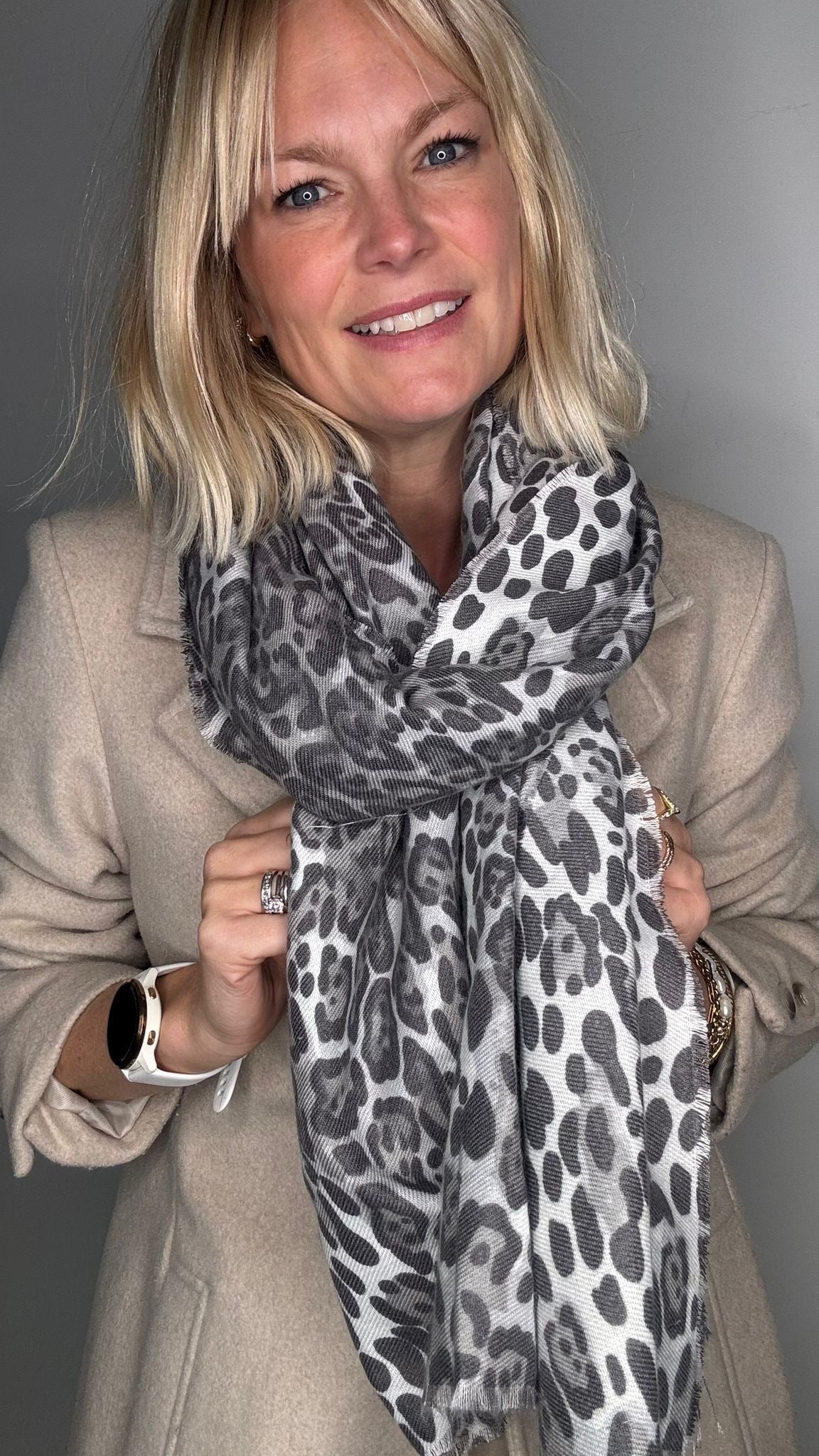 Woman wearing a beige coat and a grey animal print scarf 