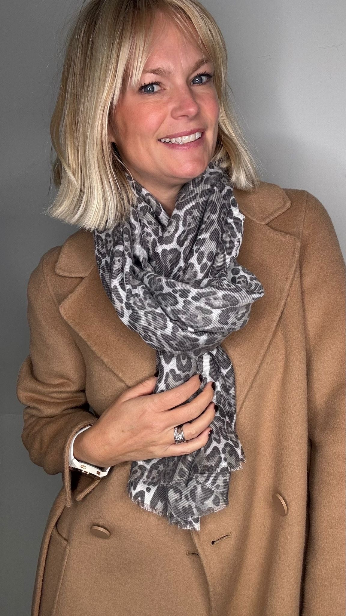 Woman wearing a tan coat and a grey animal print scarf 