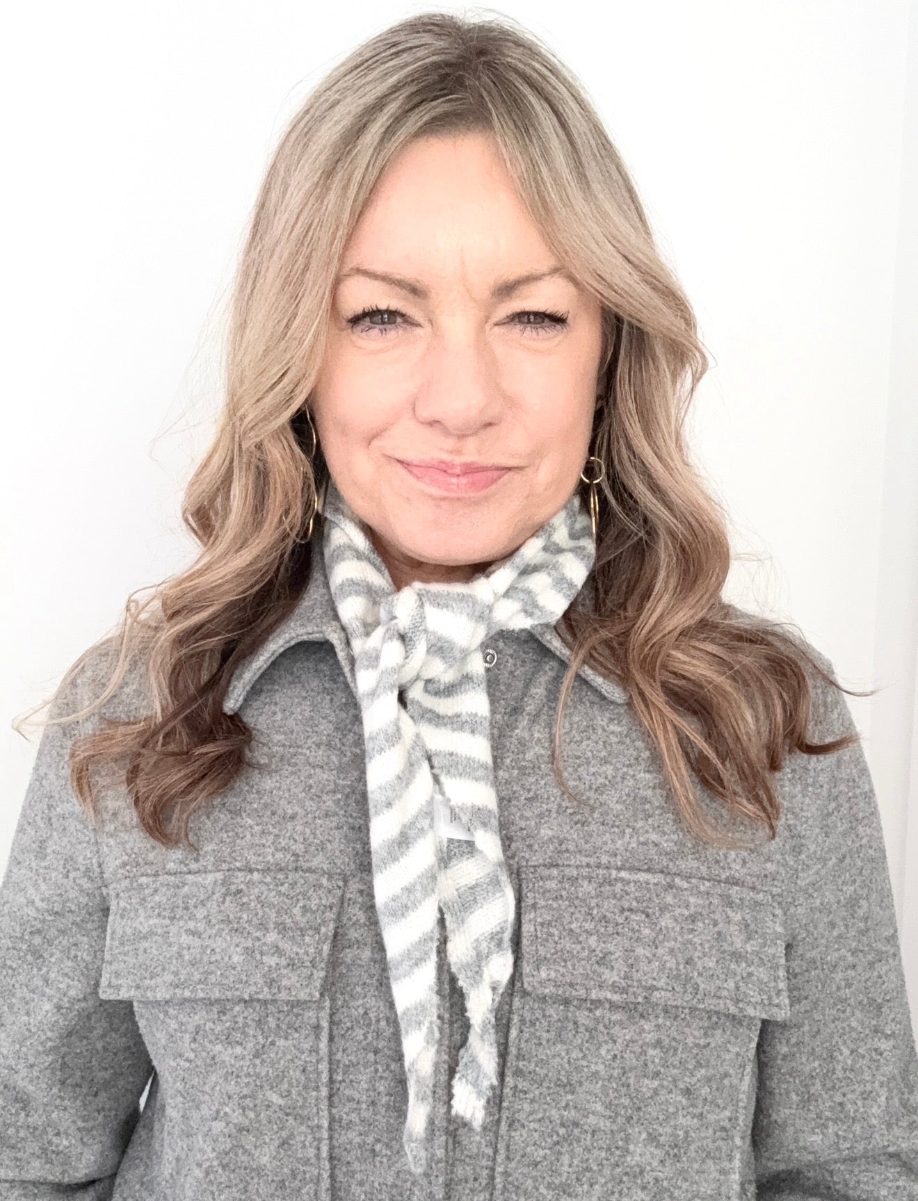 Woman wearing a grey coat and  grey and cream patterned scarf against a white background